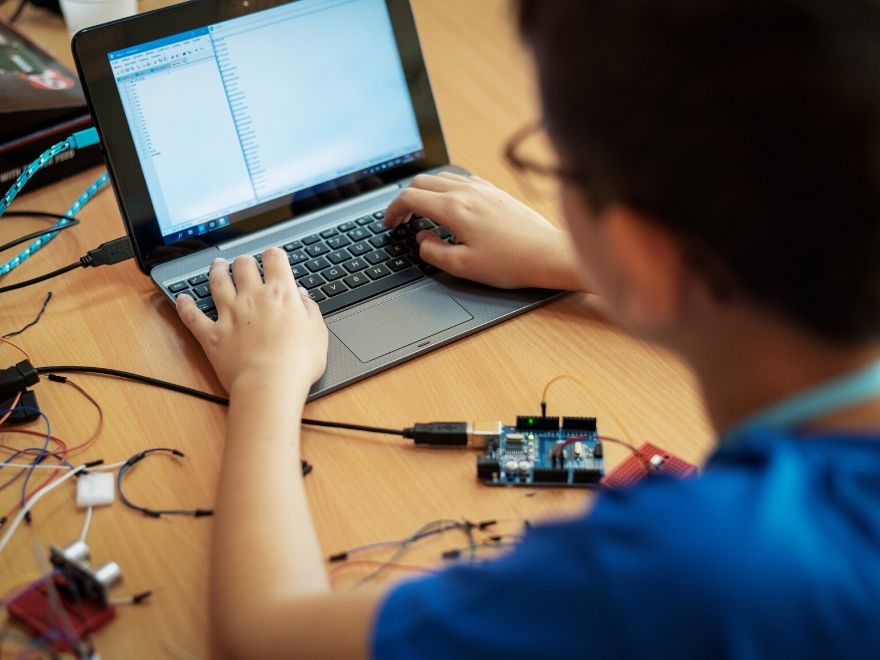 A man sitting with a laptop interfaced with a circuit board. He is using a breadboard as well.